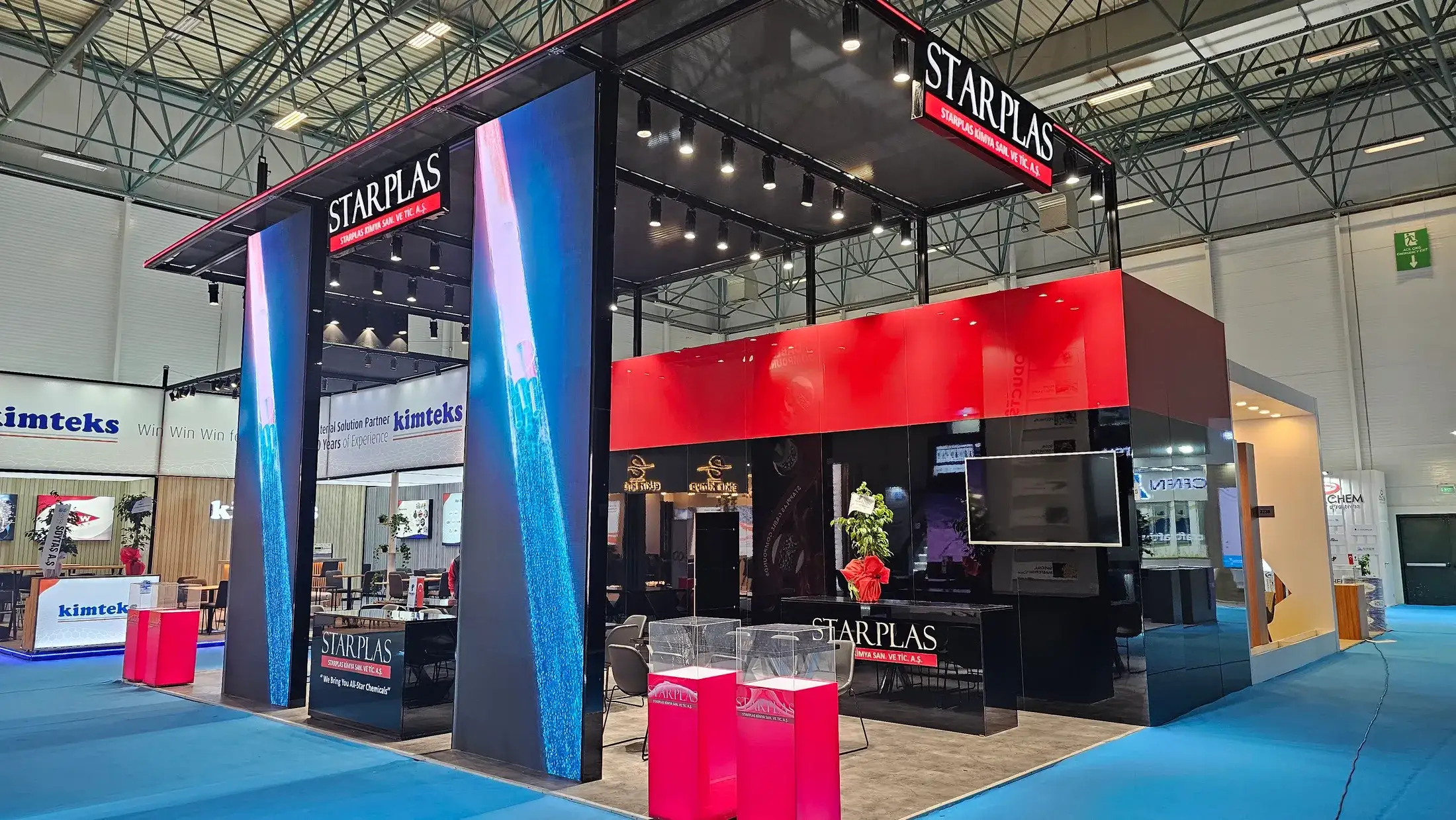 Starplas için kurulmuş fuar standı; siyah karkas, kırmızı üst blok ve iki yanda mavi görüntü veren LED totemler.